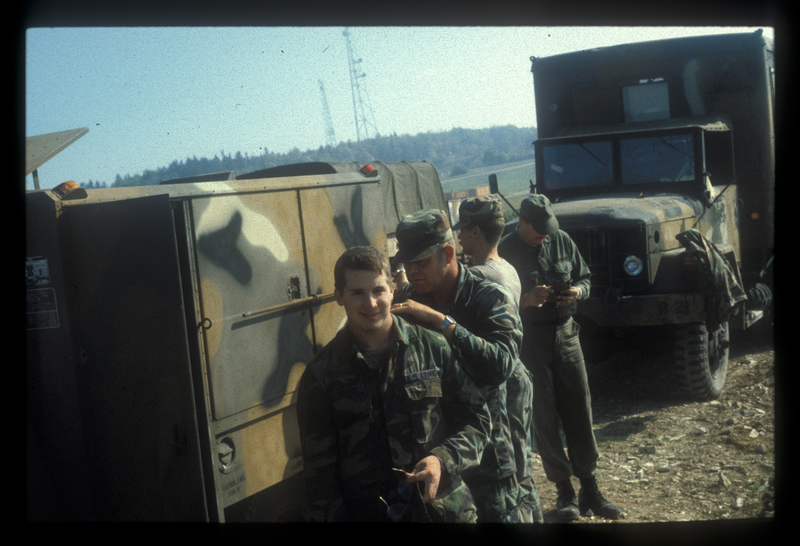 This one is in Germany. The first field exercise I participated in was a REFORGER exercise: Return of Forces to Germany. We loaded up our s**t and deployed from Louisiana to Germany. First Sergeant Robert Judd, a soulless man, is trimming my hair.